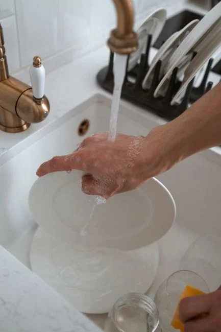 about-us-01 Person using spray bottle and cloth for cleaning a kitchen shelf, ensuring hygiene and cleanliness.