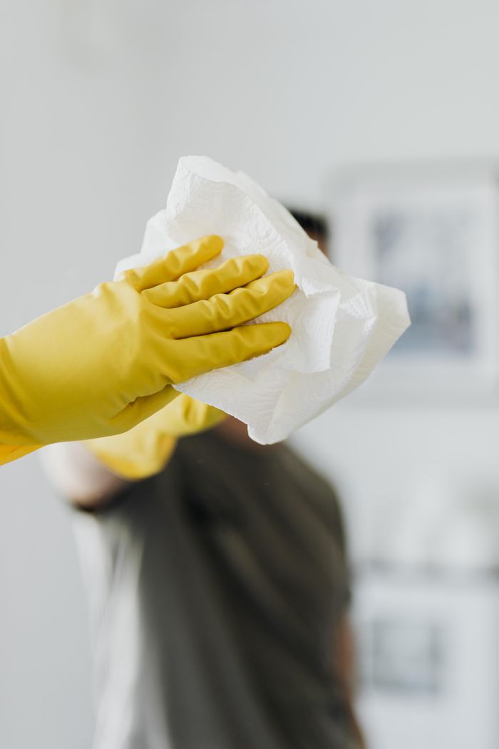 about-us-02 Anonymous male wearing yellow latex gloves and dark t shirt wiping mirror in bathroom with paper napkin